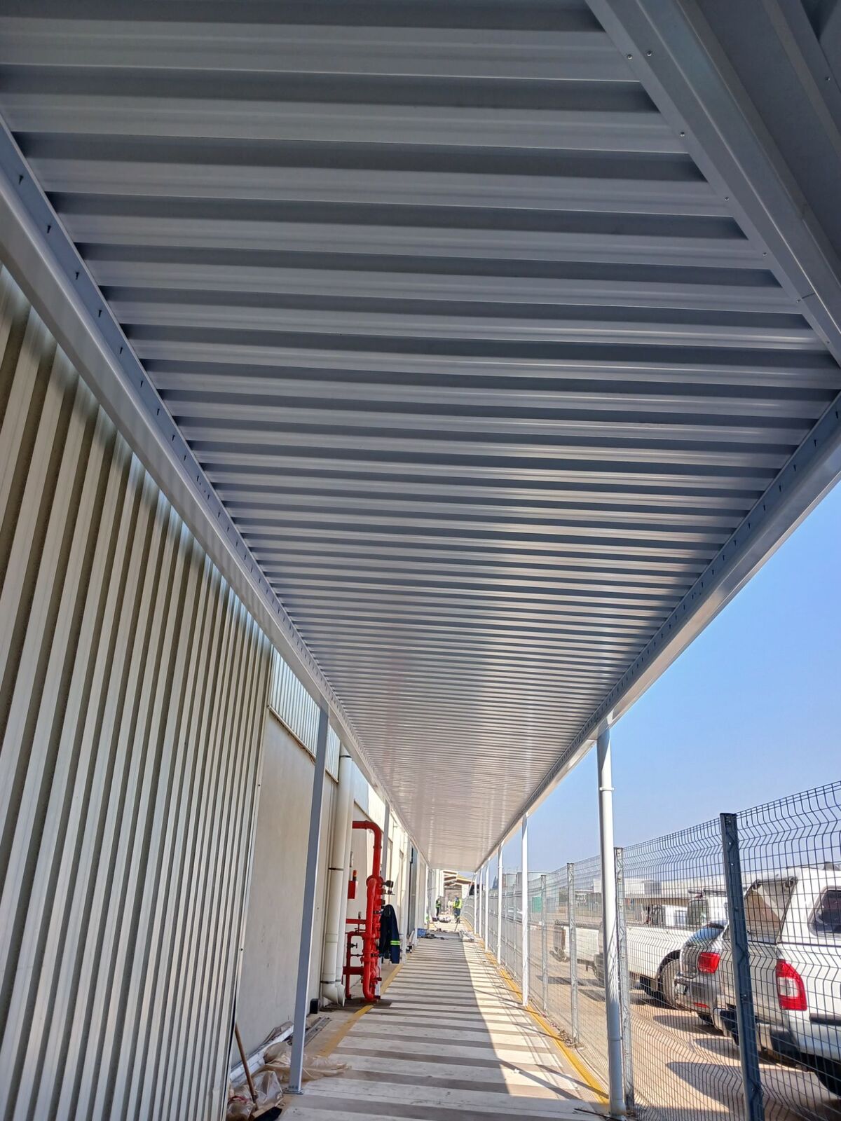 Long IBR-roofed walkway canopy on slim steel columns running alongside an industrial building