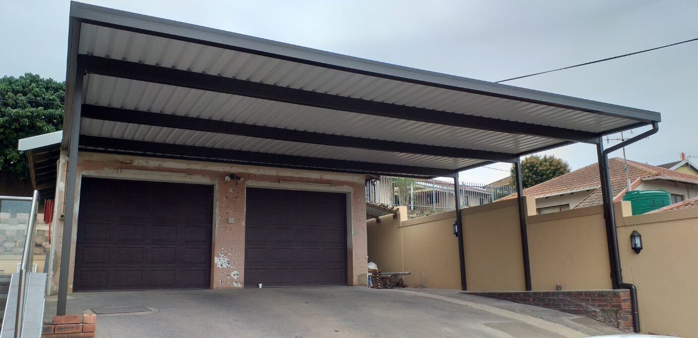 Charcoal-framed double carport with a flat IBR roof covering the driveway in front of two garages